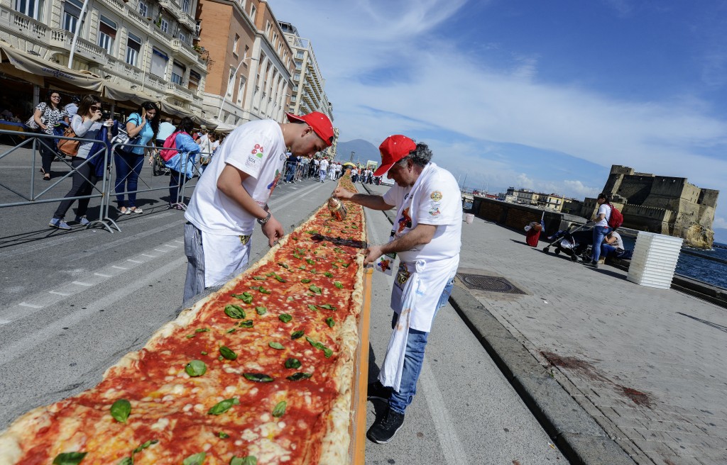 Neapolitan pizza makers attempt to make the longest pizza to break a Guinness World Record along the seafront of Naples, on May 18, 2016. For the wood-fired pizza, which measured two kilometres, they used 2,000 kg of flour, 1,600 kg of tomatoes, 2,000 kg of mozzarella, 200 litres of oil, 30kg of fresh basil. The record-breaking snack measured up at exactly 1,853.88 metres (6,082 feet), smashing the previous record of 1,595.45 metres (5,234 feet) set at last year's World Expo in Milan, Italy's food and agriculture board Coldiretti said. / AFP PHOTO / Mario LAPORTA
