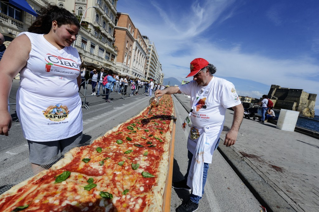 Neapolitan pizza makers attempt to make the longest pizza to break a Guinness World Record along the seafront of Naples, on May 18, 2016. For the wood-fired pizza, which measured two kilometres, they used 2,000 kg of flour, 1,600 kg of tomatoes, 2,000 kg of mozzarella, 200 litres of oil, 30kg of fresh basil. The record-breaking snack measured up at exactly 1,853.88 metres (6,082 feet), smashing the previous record of 1,595.45 metres (5,234 feet) set at last year's World Expo in Milan, Italy's food and agriculture board Coldiretti said. / AFP PHOTO / Mario LAPORTA