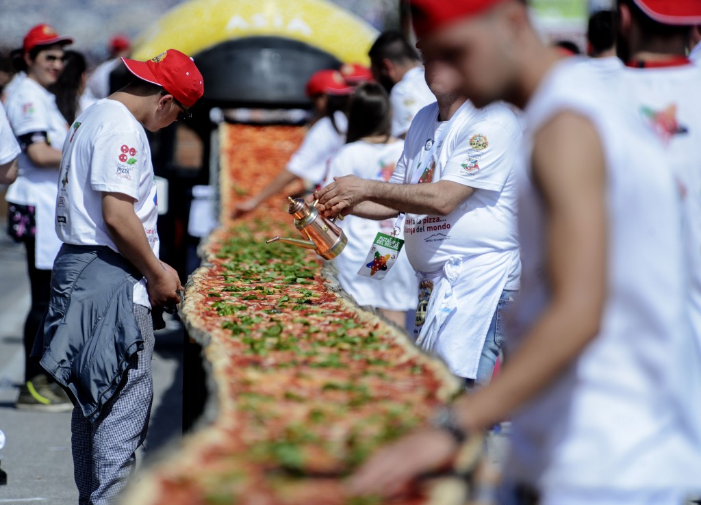 Neapolitan pizza makers attempt to make the longest pizza to break a Guinness World Record along the seafront of Naples, on May 18, 2016. For the wood-fired pizza, which measured two kilometres, they used 2,000 kg of flour, 1,600 kg of tomatoes, 2,000 kg of mozzarella, 200 litres of oil, 30kg of fresh basil. The record-breaking snack measured up at exactly 1,853.88 metres (6,082 feet), smashing the previous record of 1,595.45 metres (5,234 feet) set at last year's World Expo in Milan, Italy's food and agriculture board Coldiretti said. / AFP PHOTO / Mario LAPORTA
