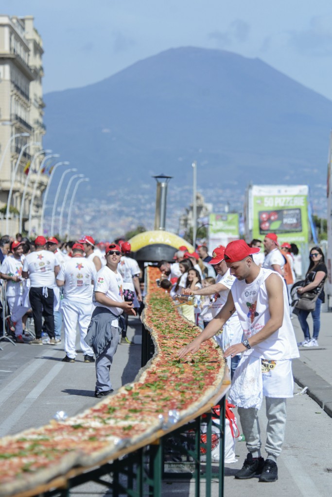 Neapolitan pizza makers attempt to make the longest pizza to break a Guinness World Record along the seafront of Naples, on May 18, 2016. For the wood-fired pizza, which measured two kilometres, they used 2,000 kg of flour, 1,600 kg of tomatoes, 2,000 kg of mozzarella, 200 litres of oil, 30kg of fresh basil. The record-breaking snack measured up at exactly 1,853.88 metres (6,082 feet), smashing the previous record of 1,595.45 metres (5,234 feet) set at last year's World Expo in Milan, Italy's food and agriculture board Coldiretti said. / AFP PHOTO / Mario LAPORTA