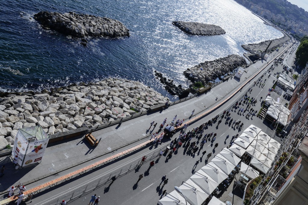 Neapolitan pizza makers attempt to make the longest pizza to break a Guinness World Record along the seafront of Naples, on May 18, 2016. For the wood-fired pizza, which measured two kilometres, they used 2,000 kg of flour, 1,600 kg of tomatoes, 2,000 kg of mozzarella, 200 litres of oil, 30kg of fresh basil. The record-breaking snack measured up at exactly 1,853.88 metres (6,082 feet), smashing the previous record of 1,595.45 metres (5,234 feet) set at last year's World Expo in Milan, Italy's food and agriculture board Coldiretti said. / AFP PHOTO / Mario LAPORTA