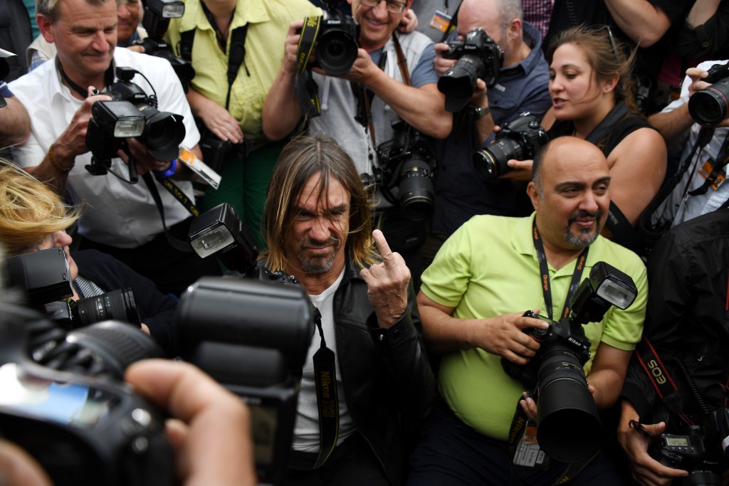 US singer Iggy Pop (C) gives the finger while posing on May 19, 2016 among photographers during a photocall for the film "Gimme Danger" at the 69th Cannes Film Festival in Cannes, southern France. / AFP PHOTO / ANNE-CHRISTINE POUJOULAT