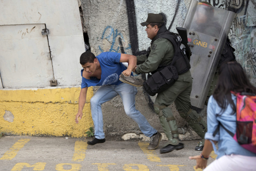 A Venezuelan government supporter scuffles with National Guard personnel in riot gear during a protest in front of the Supreme Court in Caracas on March 31, 2017. Venezuela's attorney general Luisa Ortega surprisingly broke ranks with President Nicolas Maduro on Friday, condemning recent Supreme Court rulings that consolidated the socialist president's power as a "rupture of constitutional order." / AFP PHOTO / STR